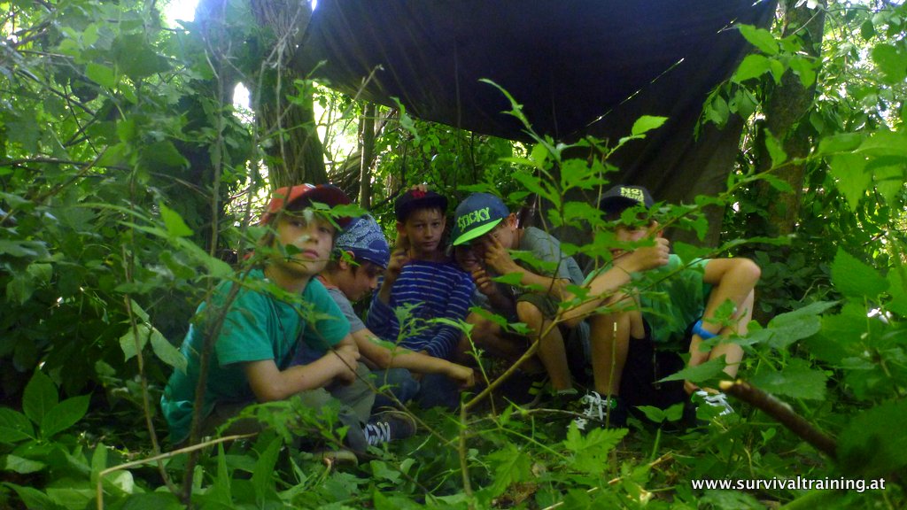 Kindergruppe unter einem selbstgebauten Unterstand im Wald