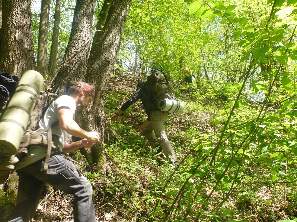 Gruppe steigt mit schweren Rucksäcken durch steiles Waldgelände